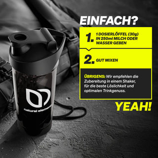 Auf einer dunklen Fläche steht eine schwarze Shakerflasche mit der Aufschrift "natural elements", daneben eine deutschsprachige Zubereitungsanleitung für eine Getränkemischung.