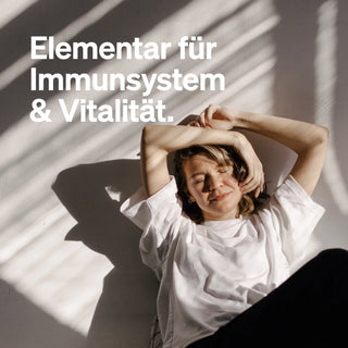 Eine Frau entspannt sich im Sonnenlicht, mit deutschem Text: "Elementar für Immunsystem & Vitalität.
